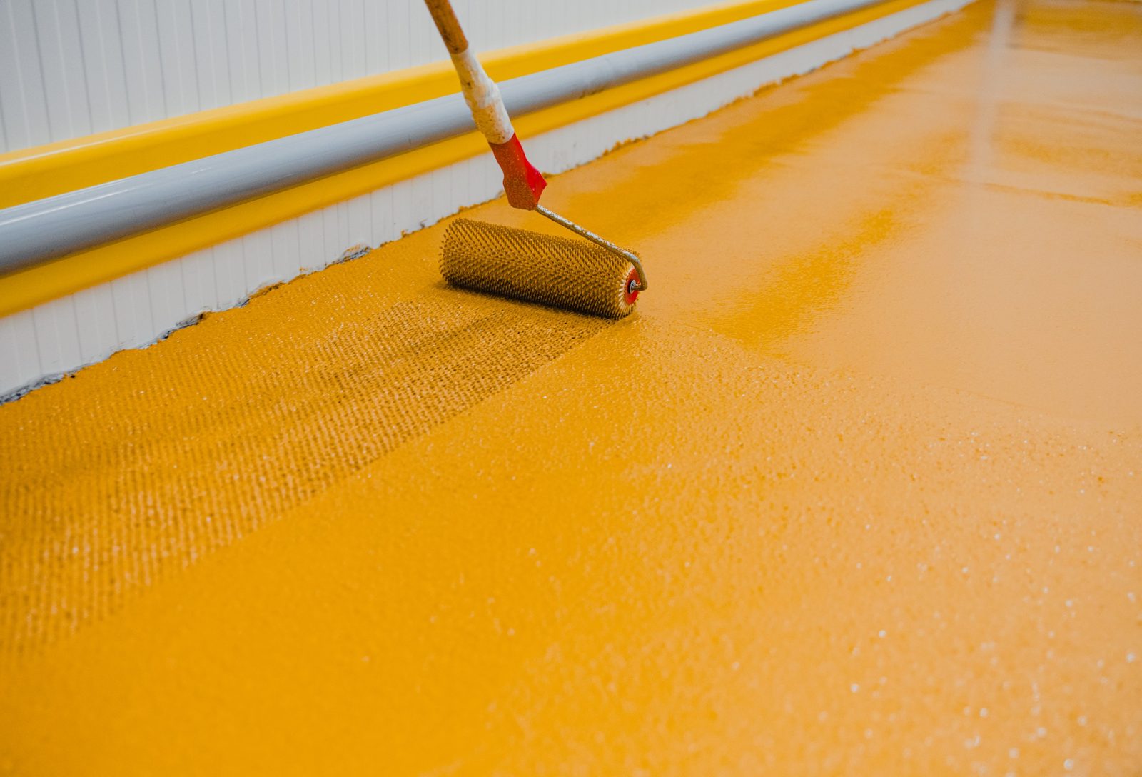 Installer pouring amber epoxy coating from a bucket onto a concrete floor