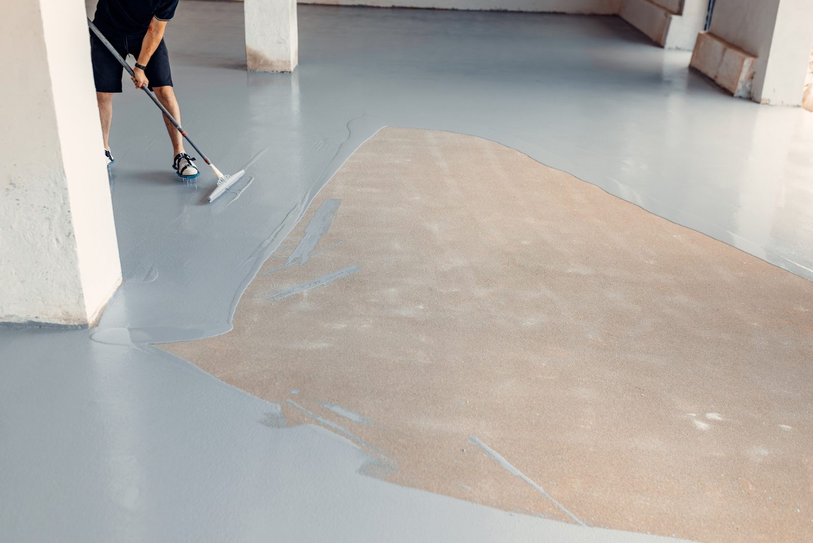 Crew leveling a fresh glossy floor coating with a squeegee while wearing spiked shoes